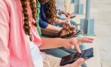 Teens sit in a row looking at their phones. 