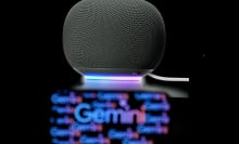  the Gemini logo is displayed on a mobile phone screen in front of a Google smart speaker