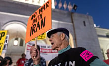 A person stands amid a crowd, holding an orange protest sign that reads "No war with Iran."
