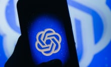 A hand in shadows holds a glowing phone, displaying a blue ChatGPT logo.