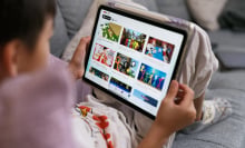 A child sits with an iPad resting on their knees. The screen shows the YouTube Kids homepage.