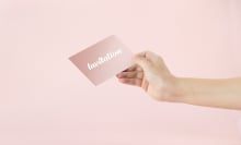 Hand holding a pink invitation card on pink background.