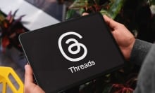 Close-up of businessman holding tablet displaying threads app logo, suggesting connection and communication in professional setting