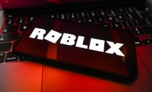 A phone displays the Roblox logo. It is photographed in harsh red light.