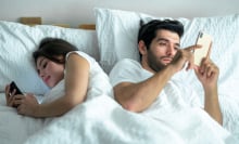 young couple using on their phones in bed back to back