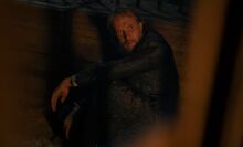 A man sits in a dark jail cell.
