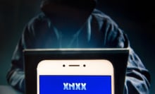 In this photo illustration, the Pornographic video sharing and viewing websites Xnxx logo is seen displayed on an Android mobile device with a figure of hacker in the background