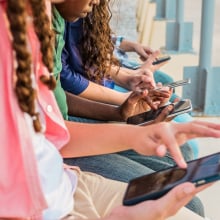 Teens sit in a row looking at their phones. 