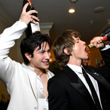 Connor Storrie and Hudson Williams, stars of Heated Rivalry, pose with bottles of champagne. 