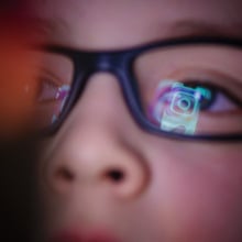 Instagram logo is reflected in boy's glasses. 