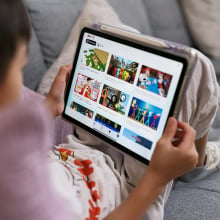 A child sits with an iPad resting on their knees. The screen shows the YouTube Kids homepage.