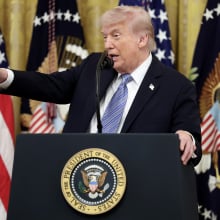 Trump stands at a White House podium pointing to the right. 