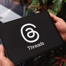 Close-up of businessman holding tablet displaying threads app logo, suggesting connection and communication in professional setting