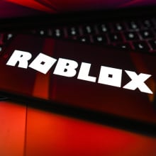 A phone displays the Roblox logo. It is photographed in harsh red light.