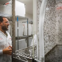 A man stands in a lab next to a metal rack holding a large enclosure filled with mosquitos.