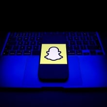 Snapchat logo on a smartphone, which is placed on an open laptop.