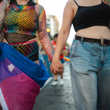 two people at pride parade, one is wrapped in the bi pride flag, another in the trans pride flag