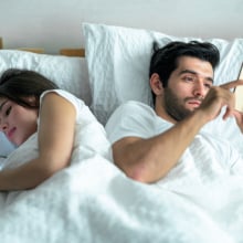 young couple using on their phones in bed back to back