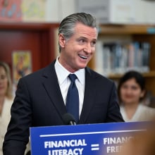 Gavin Newsom stands at a podium in the middle of a library.