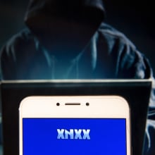 In this photo illustration, the Pornographic video sharing and viewing websites Xnxx logo is seen displayed on an Android mobile device with a figure of hacker in the background