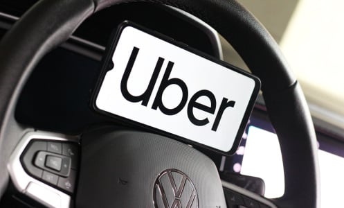 A phone showing the uber logo leans on a steering wheel.