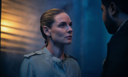 A woman stands in a room looking at a man slightly off camera.