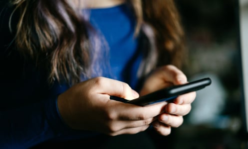A focused view of individual's hands using a mobile phone indoors, conveying technology and communication concepts.