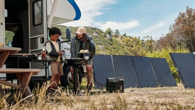 the EcoFlow Delta 2 Max portable power station at a campground in front of an RV. There are solar panels behind the EcoFlow