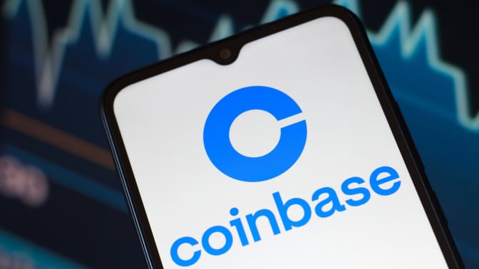 The Coinbase logo is seen displayed on a smartphone screen.