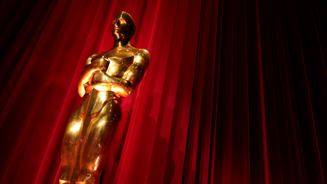 A shiny Oscar statue in front of a red curtain.