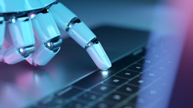 A robot hand presses a button on a laptop. 