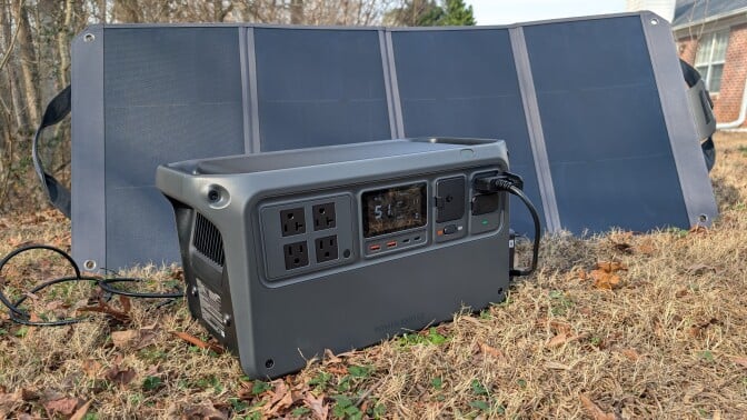 the DJI power 1000 v2 sits in a brown lawn with a solar panel behind it