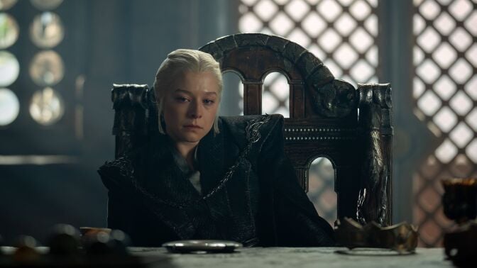 A woman sits on a chair in front of a table, looking unhappy.
