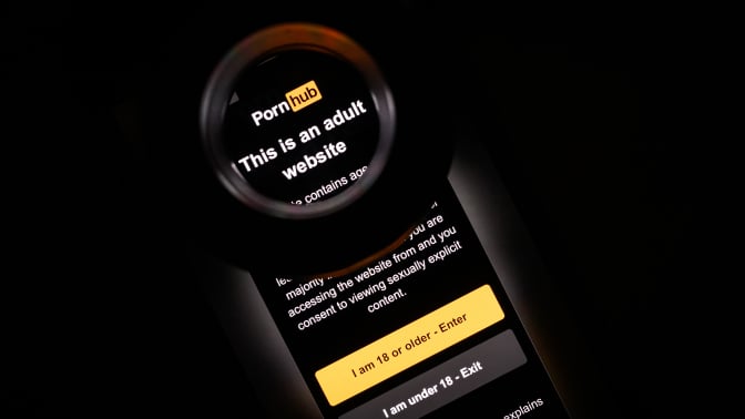 In this photo illustration, the age-restriction warning screen of the website PornHub is displayed on a digital screen