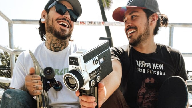 two people holding skateboards are smiling while one holds the camp snap 8 camera
