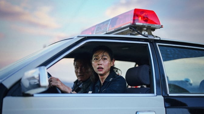 Two police officers look terrified in a police car in a still from the movie "Hope."