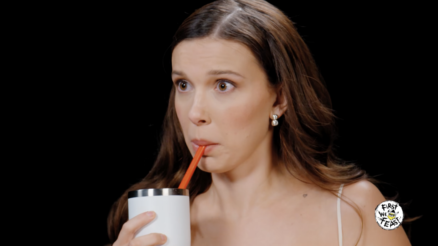 A woman sits in a dark room sipping through a straw.