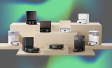 Nine Roomba robot vacuums arranged on wooden stand with gray, blue, and green backdrop