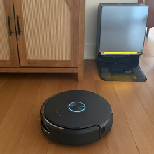 Narwal Flow 2 robot vacuum cleaning hardwood floor in front of self-empty dock and credenza