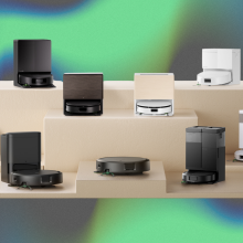 Nine Roomba robot vacuums arranged on wooden stand with gray, blue, and green backdrop