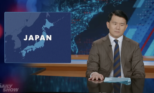 A man sits behind a talk show desk. In the top left is a world map with Japan highlighted.