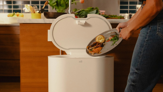 Person scraping plate of food scraps into Mill kitchen bin