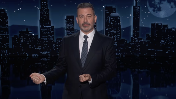 A man in a suit stands on talk show stage.