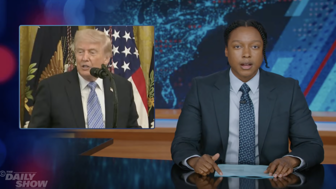 A man sits behind a talk show desk. In the top left is an image of the president.