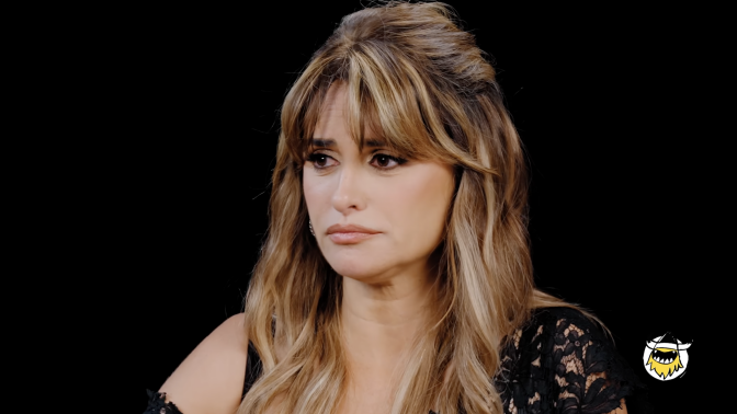 A woman sits in a dark room looking serious, with tears in her eyes.