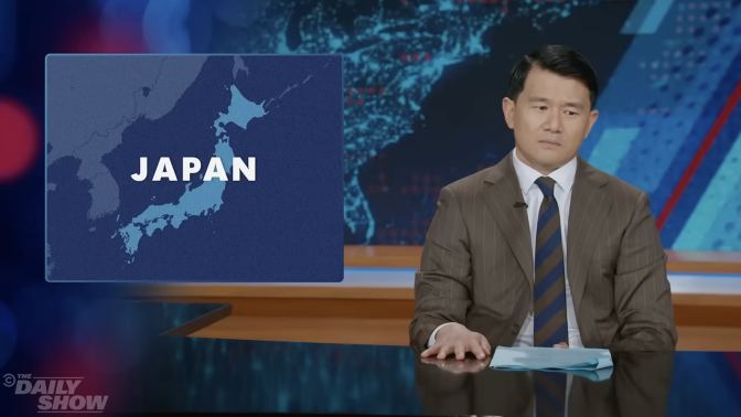 A man sits behind a talk show desk. In the top left is a world map with Japan highlighted.